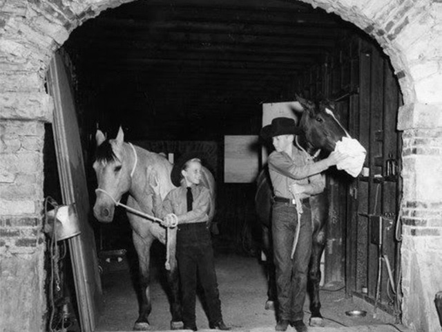 Two young boys bringing horses out of a stable